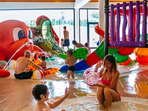 Bambini e adulti si divertono nelle **terme per bambini** con scivoli colorati e una grande attrazione a forma di polpo che spruzza acqua.