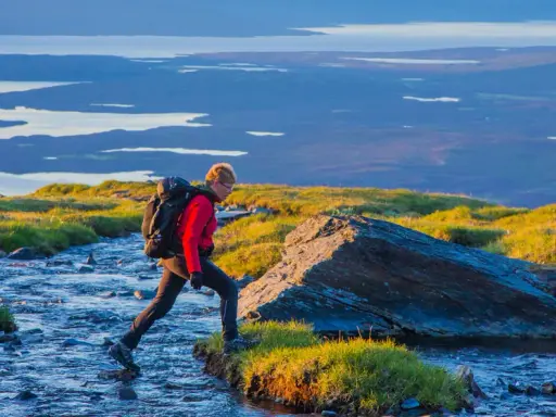 Vandrare korsar en bäck i Abisko, med Kebnekaise-massivet i bakgrunden.