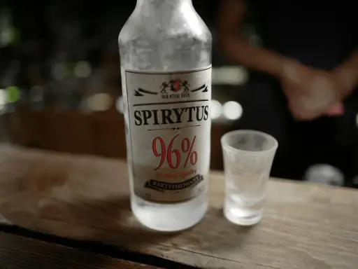 Spirytus 96% – alkohol, który ma najwięcej procent. Butelka i kieliszek na drewnianym blacie.