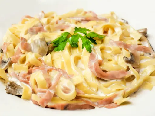 Tagliatelle z szynką i pieczarkami w kremowym sosie, ozdobione natką pietruszki. Pyszny makaron z mozzarellą w roli głównej.
