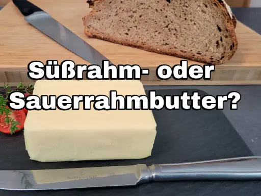 Ein Block Butter liegt neben Brot und Kräutern. Die Frage: Süßrahm- oder Sauermilchbutter?