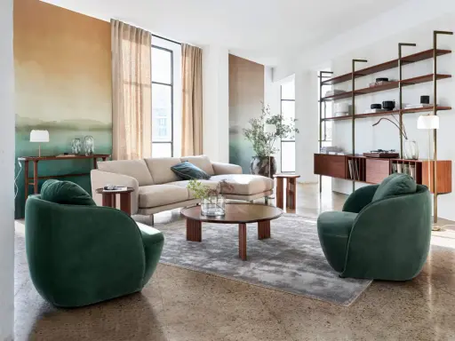 Salon au style mid century avec canapé beige, fauteuils verts velours, table basse ronde en bois et étagères murales.