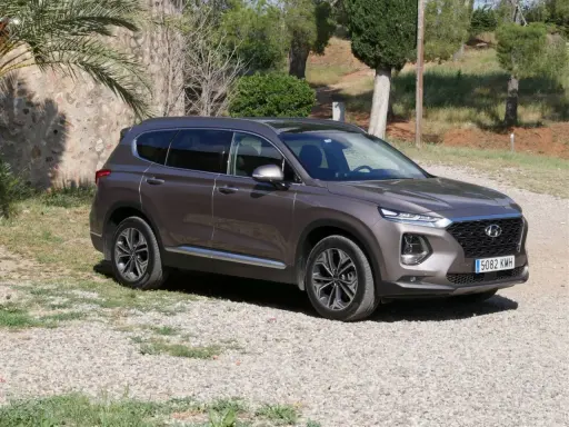 Brązowy Hyundai Santa Fe 2025 na tle kamiennego muru i zieleni.