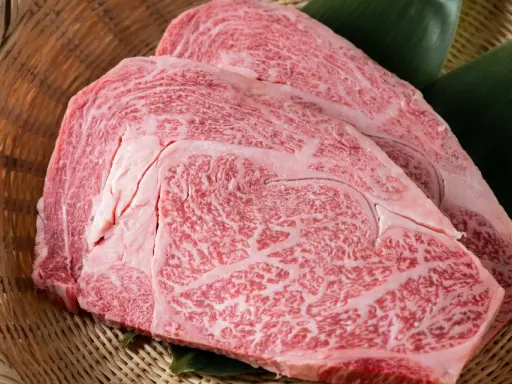 Dos cortes de carne japonesa cara, con marmoleado intenso, reposan sobre hojas verdes en una cesta de mimbre.
