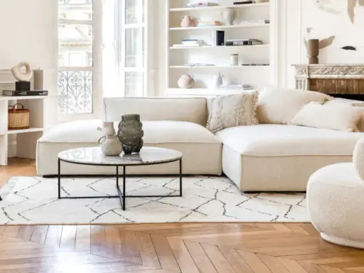 Un soggiorno luminoso con divani e design moderno. Un divano componibile bianco, una poltrona bouclé e una sedia grigia su un tappeto geometrico.