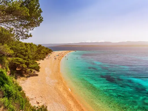Traumhafter kroatischer Strand mit Pinienwald, goldenem Sand und kristallklarem, türkisfarbenem Wasser. Menschen entspannen sich und baden.