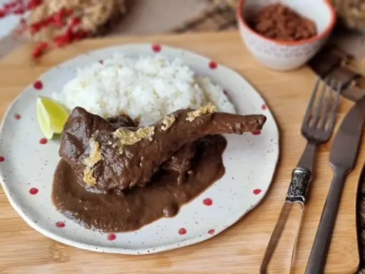 Un delicioso conejo guisado en mole oscuro, servido con arroz blanco y una rodaja de limón.