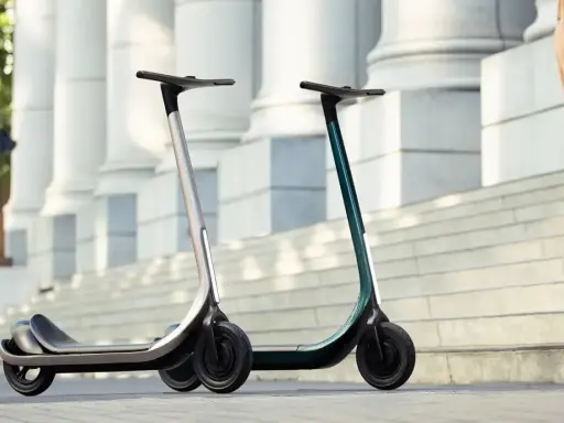 Deux trottinettes électriques modernes, idéales pour votre application trajet trottinette. L'une argentée, l'autre vert émeraude, sur des marches devant des colonnes.