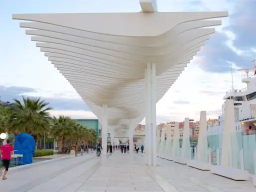Passeggiata moderna al malaga porto, con palme, una nave bianca e un cielo nuvoloso.