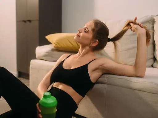 Kobieta w sportowym stroju odpoczywa po treningu, pijąc napój. Czas na regenerację mięśni i relaks.