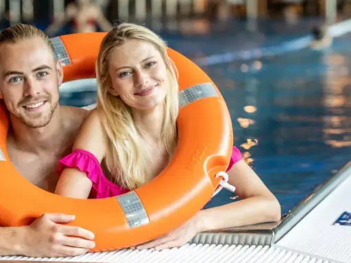 Uśmiechnięta para w basenie, trzymająca koło ratunkowe. Idealny weekend z przyjaciółką, pełen relaksu i zabawy w wodzie.