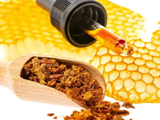 Propolis co to? Złocisty płyn z pipety i grudki propolisu na drewnianej łyżce obok plastrów miodu.