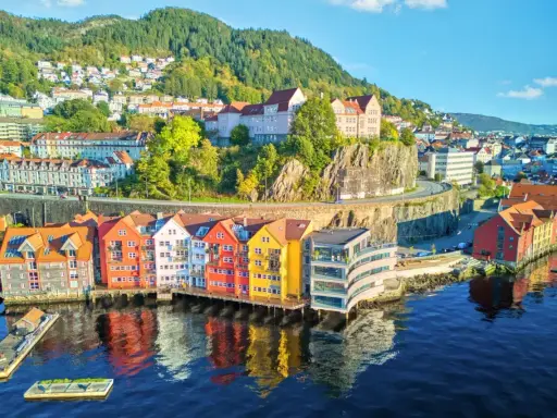 Kolorowe domy nad wodą w Bergen, idealne na norwegia zwiedzanie. W tle wzgórza porośnięte drzewami.