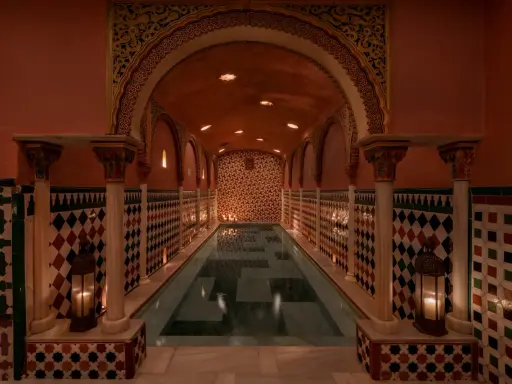 Ein prachtvoller Hammam in Granada mit einem langen Pool, umgeben von kunstvollen Kacheln und Säulen, beleuchtet von Kerzen.