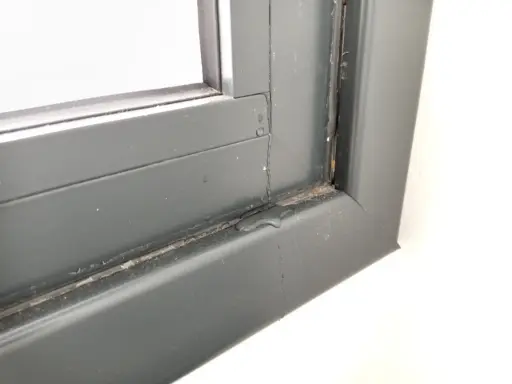Gotas de lluvia resbalan por el marco de una ventana gris, dejando un rastro húmedo.