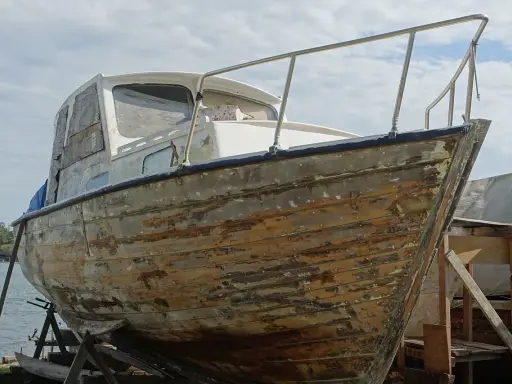 Bateau en bois sur cale, prêt à être restauré. Il faudra le nettoyer avant de naviguer sans antifouling.