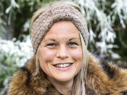 Glad kvinna med virkat pannband med twist och pälskrage, ute i naturen.