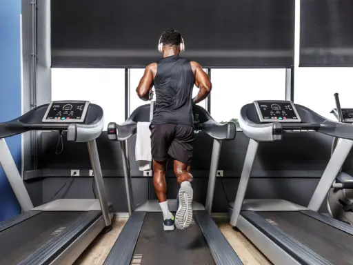 Mann mit Kopfhörern absolviert ein intensives Laufband Training in einem modernen Fitnessstudio.