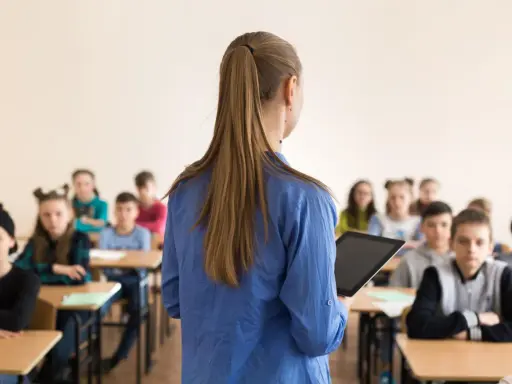 Lehrerin mit Tablet vor Schülern. Die Frage "wie viel verdient ein lehrer" beschäftigt viele.