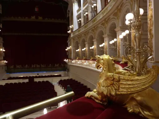 Interno del Teatro Galli di Rimini, con poltrone rosse, palchi dorati e una sfinge alata in primo piano.