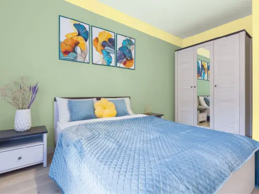 Dormitorio con paredes verde menta y detalles amarillos en el techo. Cama azul, mesita de noche y armario blanco. Inspiración de colores para pintar un dormitorio pequeño.