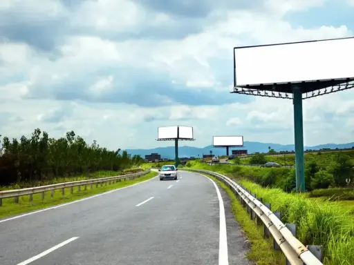 Pusta reklama przy drodze na terenie prywatnym, z widokiem na zakrzywioną autostradę i zielone wzgórza.