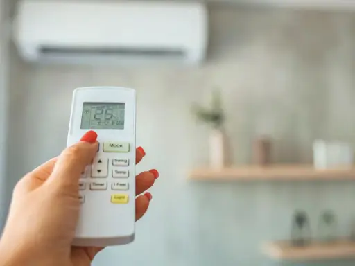 Mano con control remoto de aire acondicionado, ajustando el modo dry para dormir. La pantalla muestra 25°C.