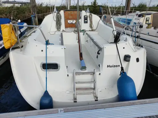 Vue arrière d'un voilier blanc amarré, avec le nom "Huizen" écrit sur la coque. Une échelle de bain est visible, ainsi que des pare-battages bleus. Le premier des 265 avis est prêt à être lu.