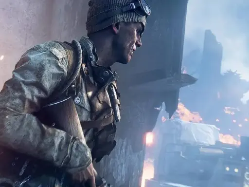 Żołnierz w czapce i goglach, gotowy do akcji w jednej z najbardziej realistycznych gier fps. W tle płonące ruiny i dym.