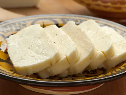 Pokrojony w plastry domowy ser halloumi na ozdobnym talerzu.