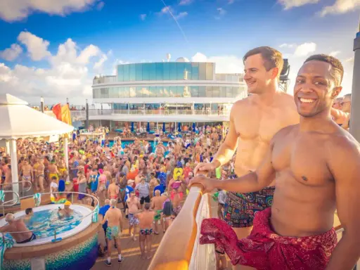 Two men smile on a cruise deck, surrounded by a lively crowd enjoying a pool party. These scenes are typical of positive gay cruises reviews.