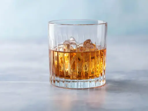 Ein Glas mit bernsteinfarbenem Getränk und Eiswürfeln, das an einen French Connection Cocktail erinnert.