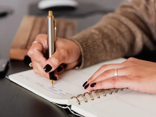 Dłoń z ciemnym lakierem pisze w notatniku. Może to lista zadań, a może spis potencjalnych poręczycieli dla kredytu?
