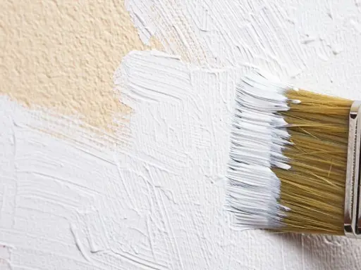 Un pinceau applique de la peinture blanche sur un mur texturé, comme une pierre de chaux.