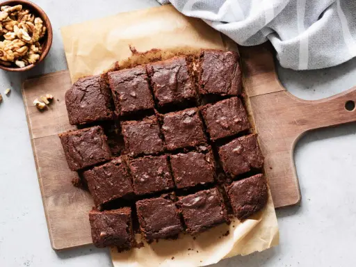 Brownies au chocolat coupés en carrés sur une planche en bois, accompagnés de noix. Un délicieux dessert healthy.