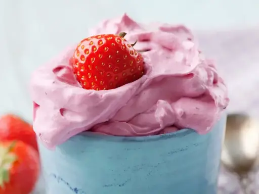 Puszysty, różowy krem z mascarpone z truskawką na wierzchu, podany w niebieskim naczyniu.