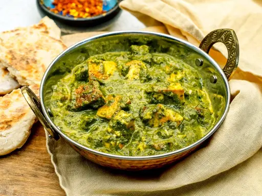 Ein köstliches Palak Paneer in einer traditionellen Schüssel, serviert mit Fladenbrot und Gewürzen.