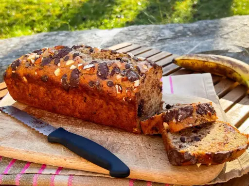 Delizioso banana bread vegano con gocce di cioccolato e mandorle, pronto per essere gustato all'aperto.