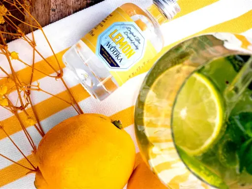 Erfrischende Vodka Cocktails mit Zitrone, Minze und Limette. Eine kleine Flasche Lemon Wodka liegt neben frischen Zitronen und gelben Blumen.