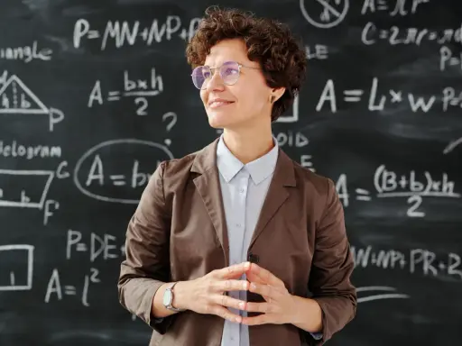 Lehrerin vor Tafel mit Matheformeln. Sie fragt sich, wie viel verdienen Grundschullehrer.