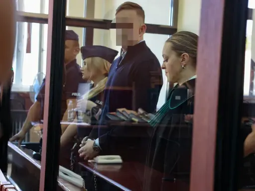 Osoba w kajdankach, prawniczka i policjanci w sali sądowej.