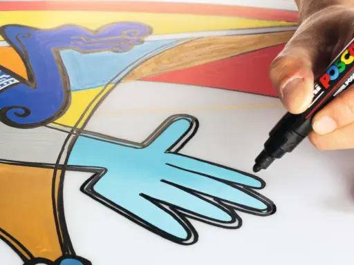 En hand använder en svart Posca-penna för att måla med posca pennor på en färgglad, abstrakt illustration.