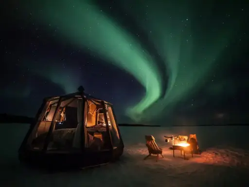 Drömmen att bo i igloo och se norrsken blir verklighet. En glaskupol med säng och en mysig eldstad utomhus under en magisk himmel.