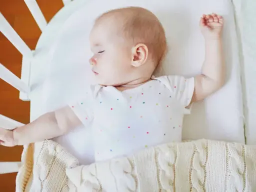 Baby schläft im Gitterbett, das Baby bewegt sich viel im Schlaf und streckt die Arme aus.