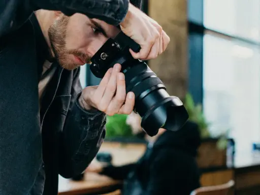 Mężczyzna z brodą w czarnej kurtce trzyma aparat, gotowy do uchwycenia chwili w stylu street photography.