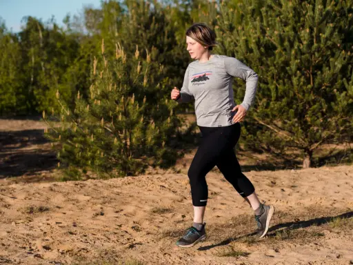 Frau beim **trail running** auf sandigem Untergrund, umgeben von Kiefern und Bäumen.