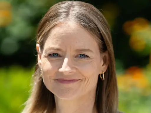 Porträt einer Frau mit blauen Augen und braunem Haar, das einige einzelne graue Haare abdeckt. Sie trägt goldene Ohrringe.