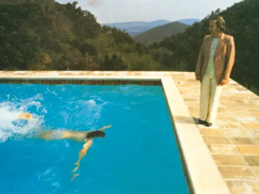 A portrait of an artist by a pool with two figures. One figure swims in the bright blue water, while another stands on the tiled edge, looking out at the mountainous landscape.