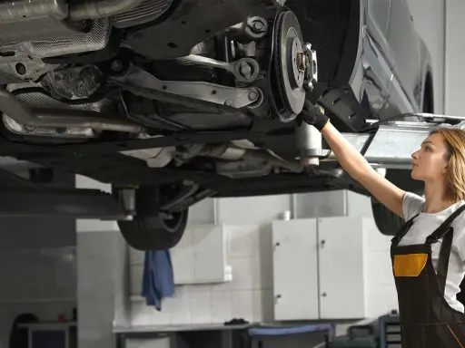 Mechaniczka sprawdza układ napędowy samochodu na podnośniku.