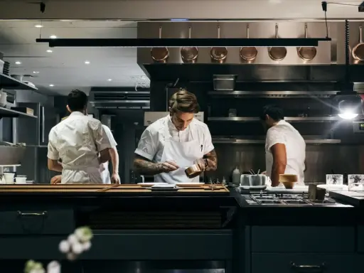 Chefs in a professional kitchen, one plating food.